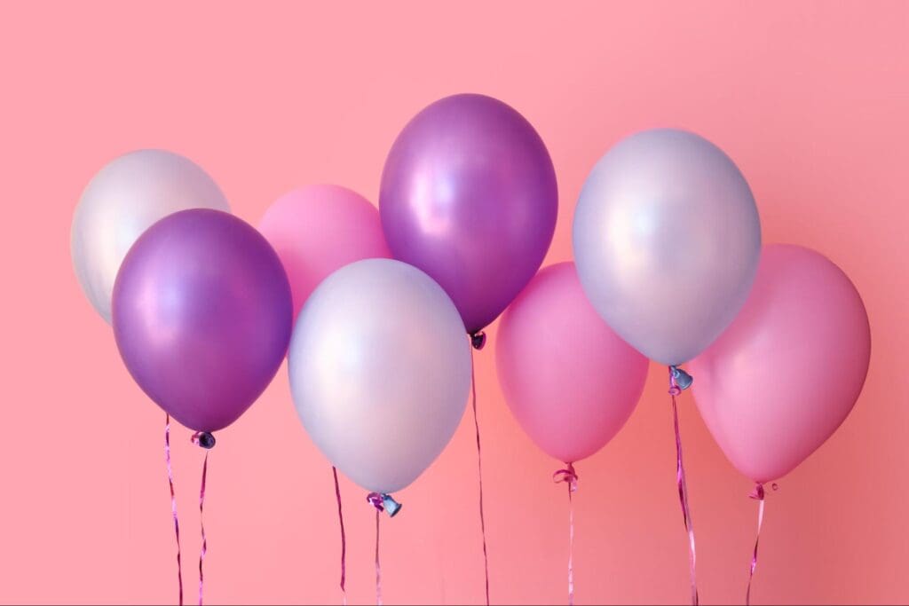 A collection of pink, purple, and white balloons floating, tied with ribbons, ideal for a celebration background.