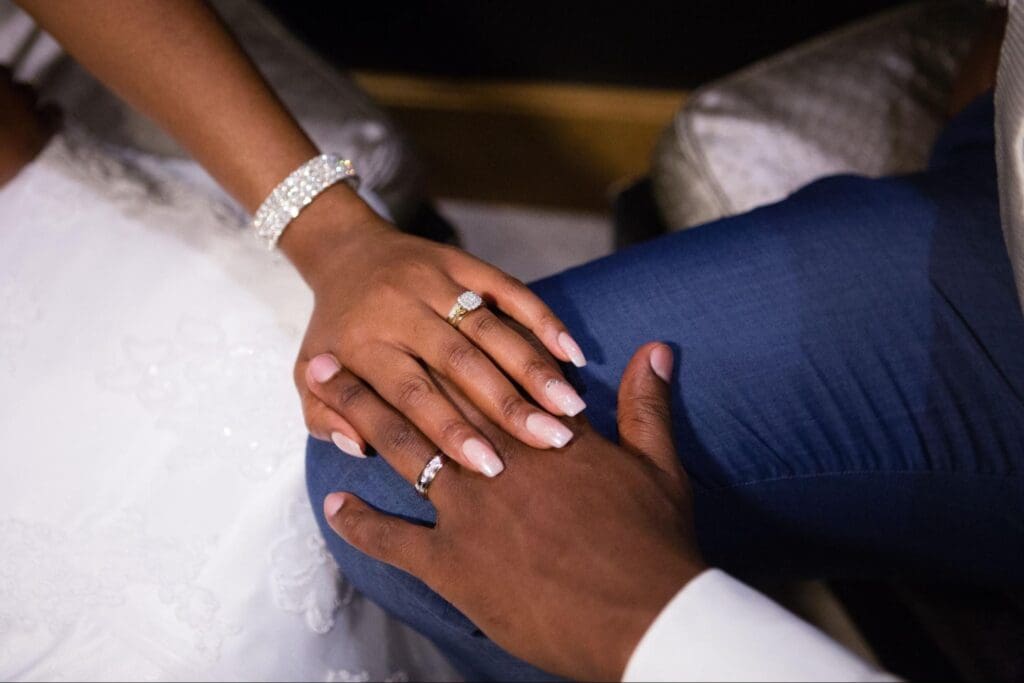 Close-up of a couple's hands with wedding rings, the bride's hand adorned with a diamond ring and bracelet, resting on the groom's hand.