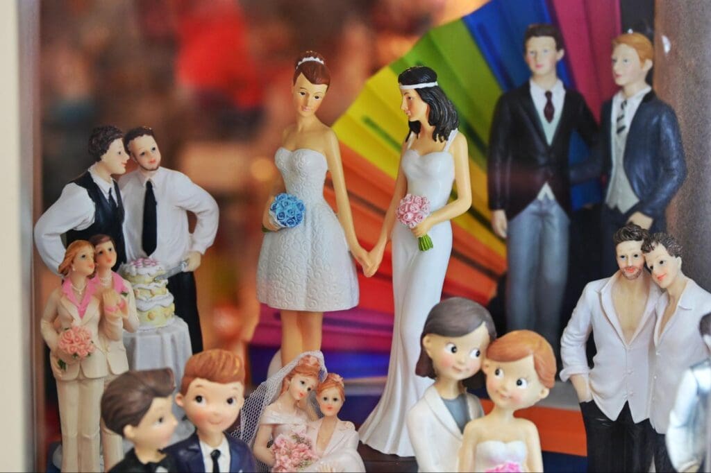 Display of various wedding cake toppers featuring different couples, including same-sex couples, holding hands and standing together.