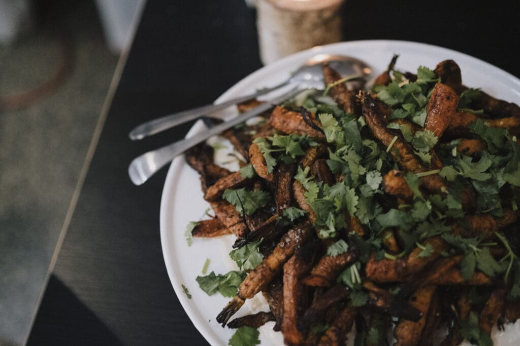 A plate of roasted carrots garnished with fresh cilantro, served with a spoon and fork on the side.