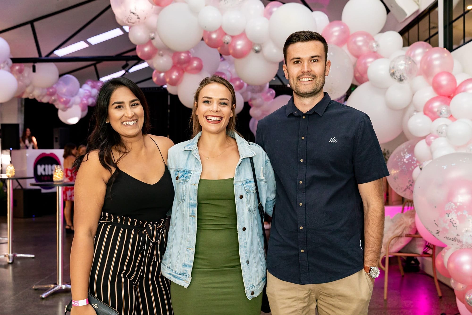 Two people and a woman stand together in front of colorful balloons, symbolizing teamwork and workplace collaboration.