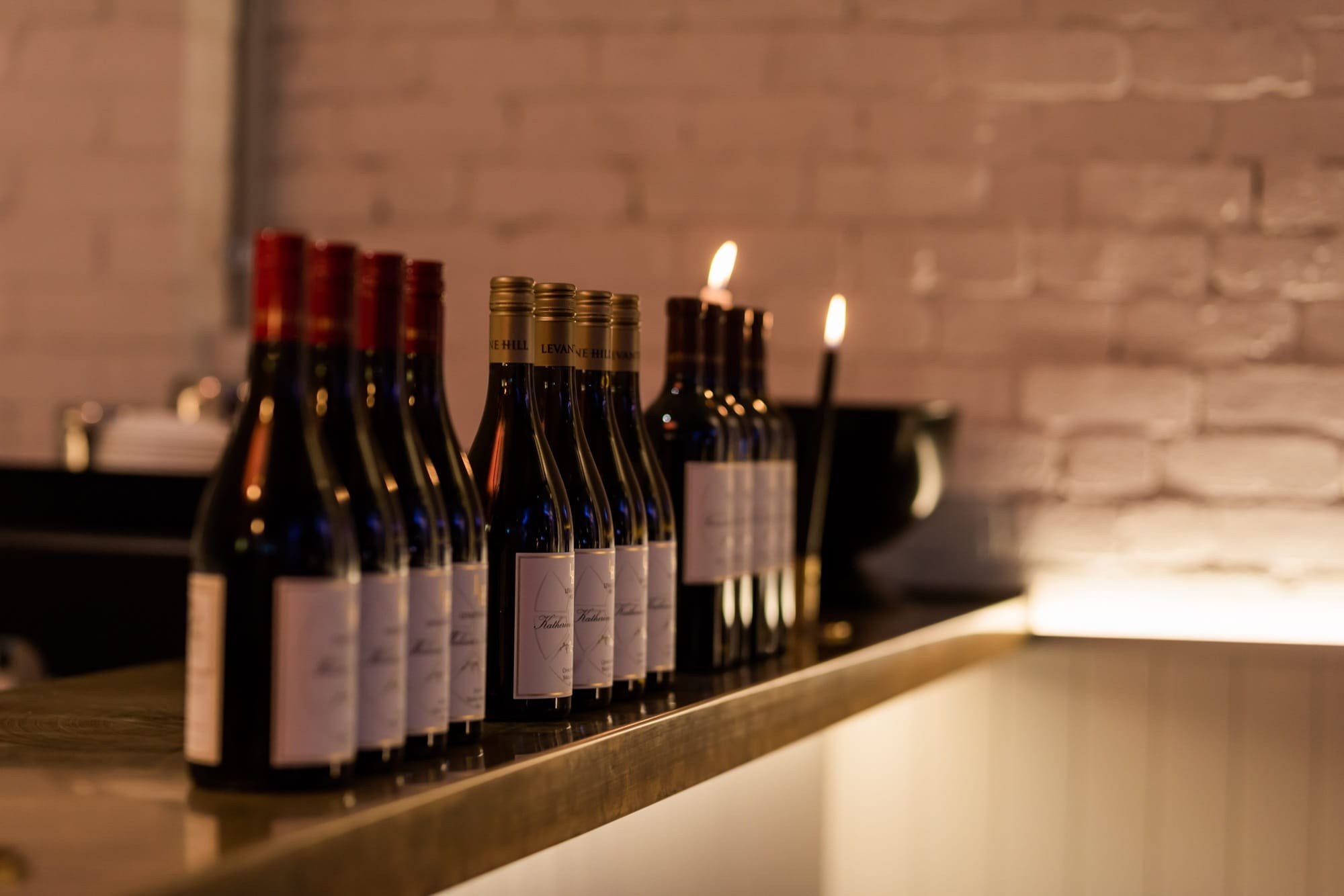 Wine bottles arranged on a counter against a rustic brick wall, highlighting hidden wedding costs related to alcohol.