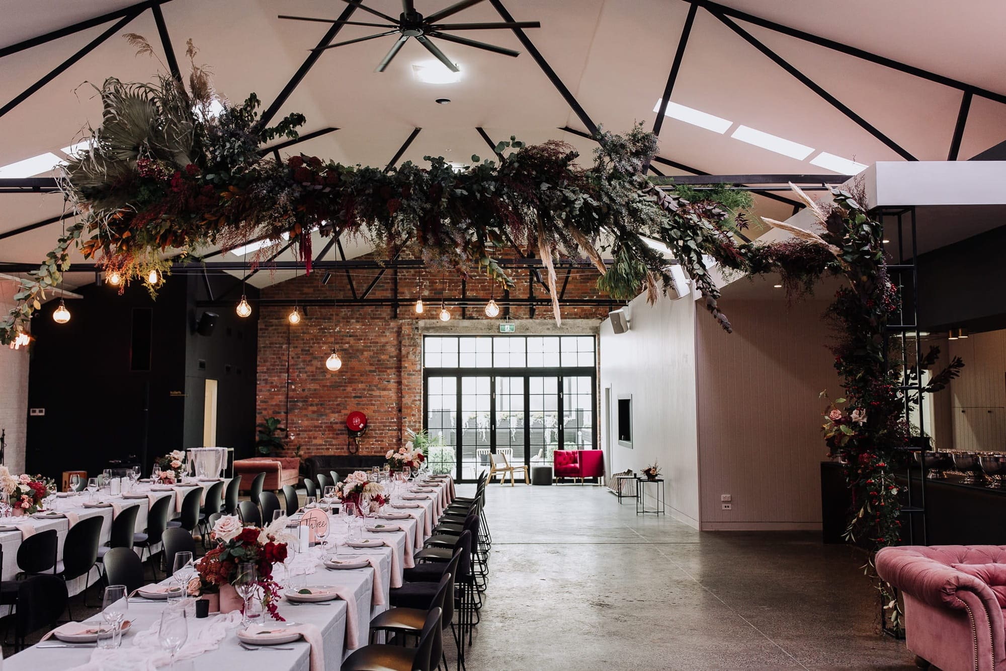 A large warehouse set for a wedding reception, adorned with pink chairs and flowers, emphasizing hidden wedding expenses.