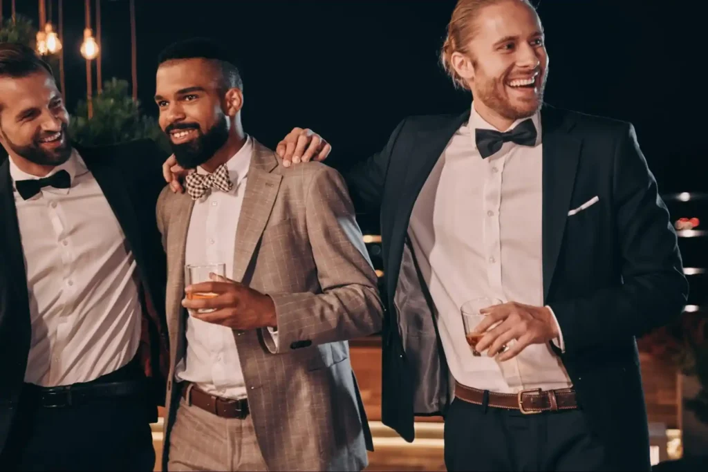 Three friends in formal suits, enjoying drinks and sharing laughter, creating a relaxed and stylish atmosphere at an evening event.