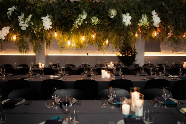 Elegantly decorated event with dinner tables, featuring hanging greenery and illuminated candles for a sophisticated atmosphere.