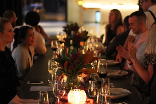 Group of guests smiling and chatting around a beautifully set dinner table, featuring floral arrangements and soft lighting.