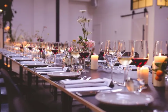 Long dinner table setup with wine glasses, floral centerpieces, and candles, creating a warm and inviting ambiance.