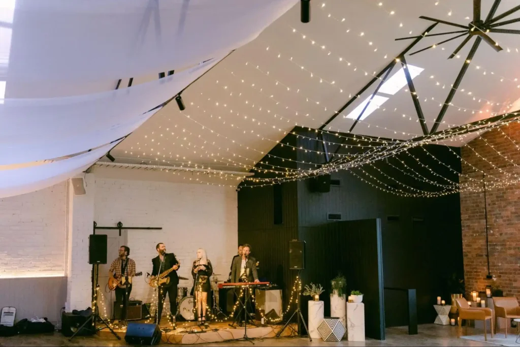 Live band performing under string lights in a decorated venue.