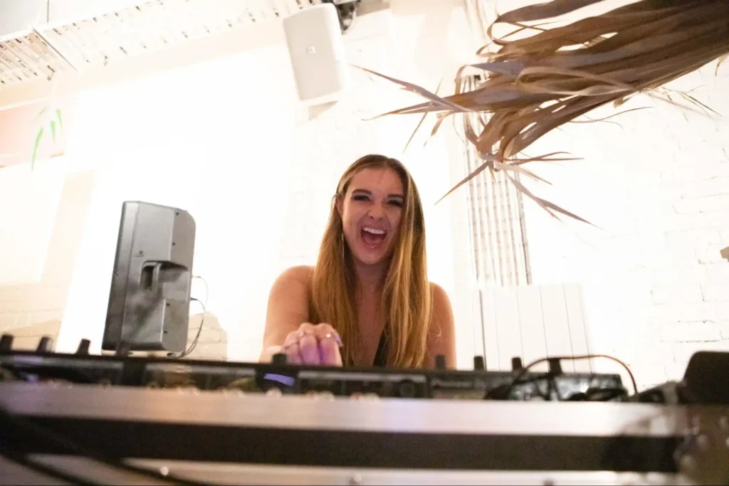 Female DJ smiling while performing at a lively event.