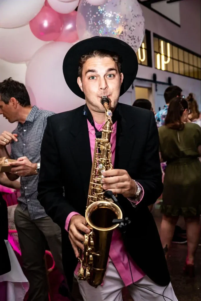 Saxophonist in a black hat playing live at an event with pink decorations.