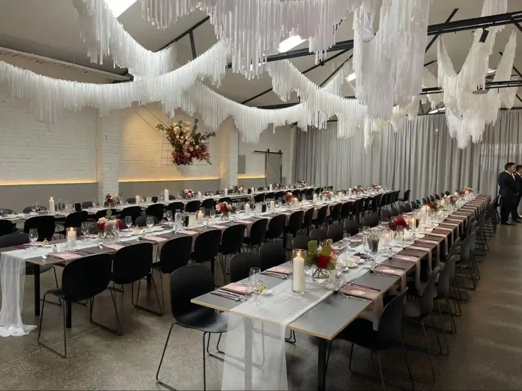 A beautifully decorated wedding dining hall with long tables and hanging white drapes.