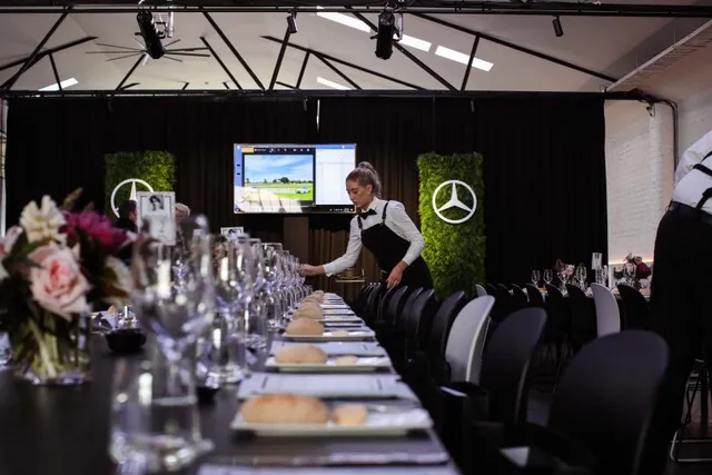 Waitstaff preparing a formal dining table with a Mercedes-Benz backdrop.