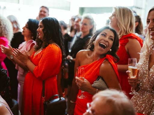 A cheerful group of women in red dresses laughing, representing a festive spirit for corporate lunch catering inspiration.