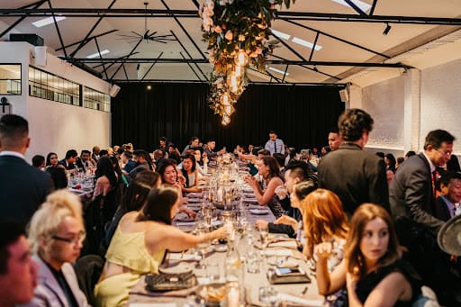 A large group of people enjoying a luxurious long lunch at long tables, surrounded by elegant decor and dining settings.