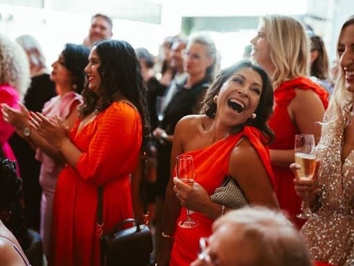 A group of women in red dresses joyfully laughing together, enjoying a fun moment at a social gathering.