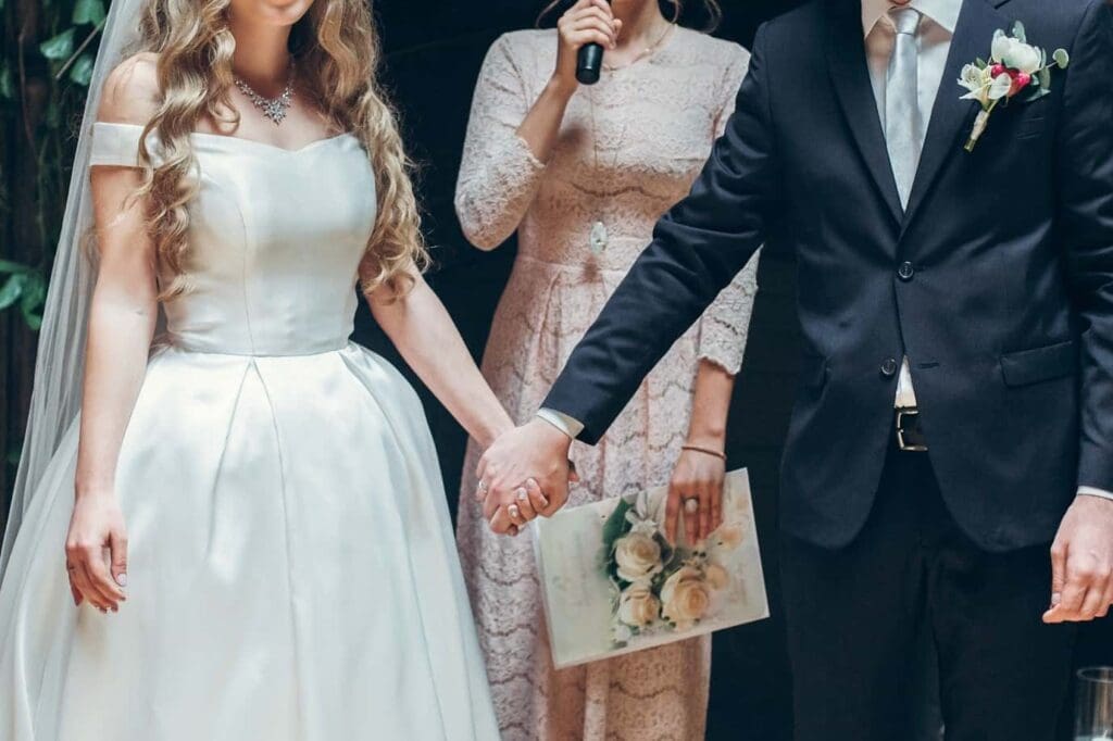 A bride and groom holding hands, gazing at each other during their wedding ceremony, surrounded by floral decorations. 